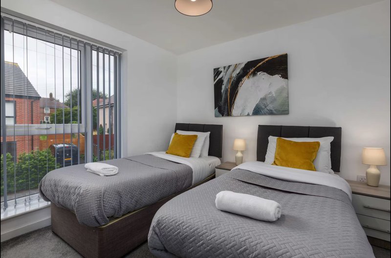 Twin bedroom with two single beds, yellow cushions, bedside lamps and patio doors overlooking garden