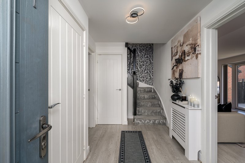 Bright hallway with white doors, wooden flooring, staircase visible, and framed wall art