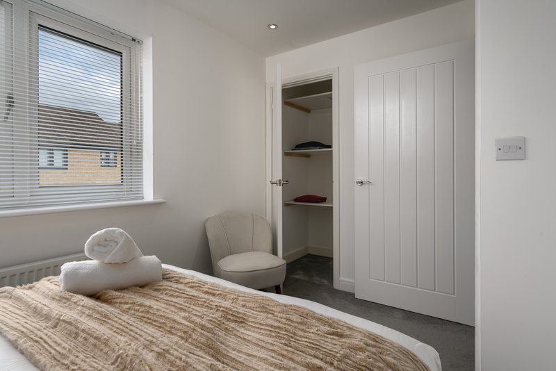 Modern bedroom with double bed, neutral bedding, cream chair, and built-in wardrobe