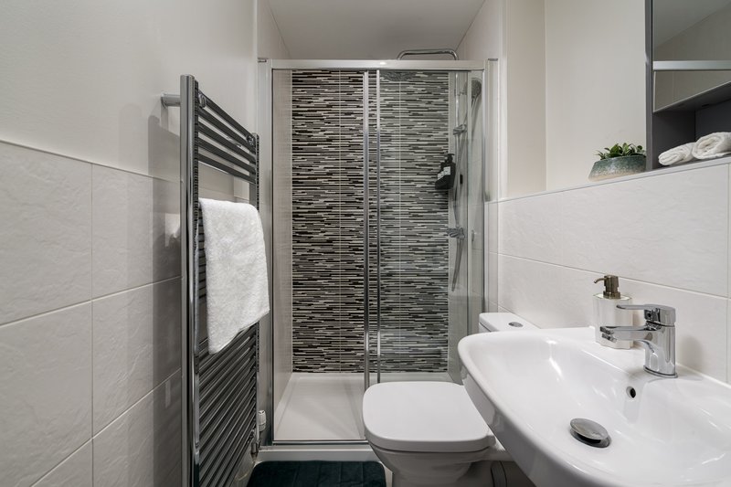 Modern bathroom with white tiles, walk-in shower, toilet, and white sink