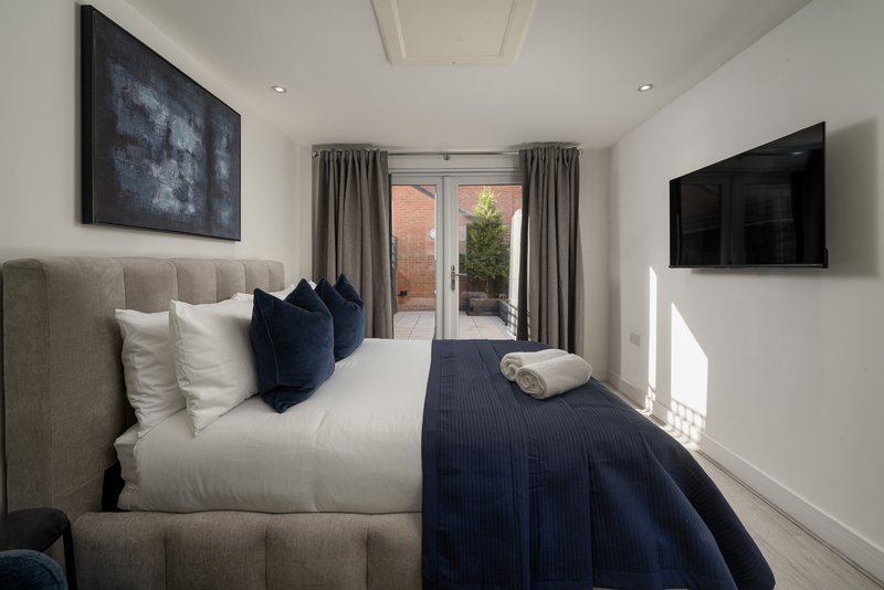 Modern bedroom with double bed, navy bedding, grey headboard, wall-mounted TV and garden view