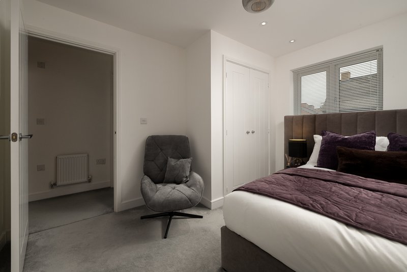 Modern bedroom with double bed, armchair, ensuite door and window with blinds