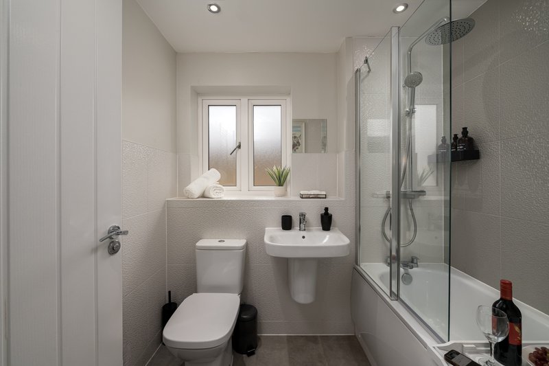 Modern bathroom with toilet, pedestal sink, glass shower enclosure and window
