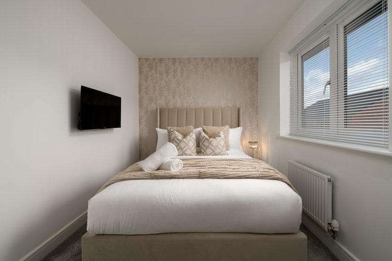 Modern bedroom with double bed, wall-mounted TV, and large window with blinds