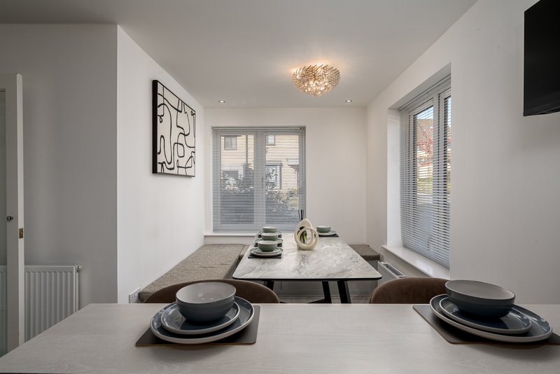 Modern dining area with two place settings, pendant light and windows overlooking garden