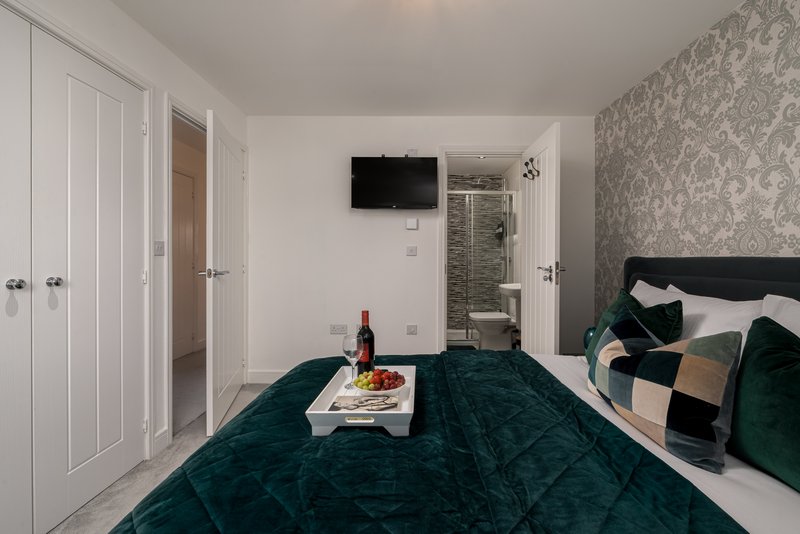 Modern bedroom with double bed, teal velvet bedding, wall-mounted TV, and ensuite bathroom