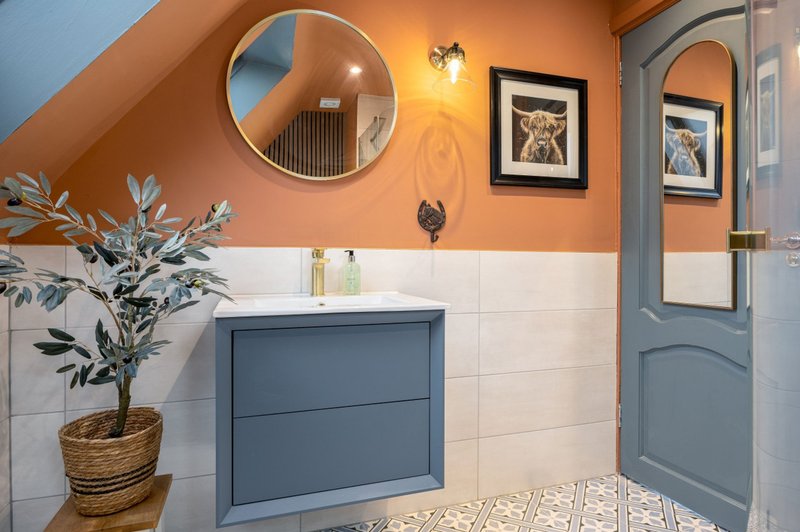 Modern bathroom with orange walls, blue vanity, round mirror, potted plant and framed artwork
