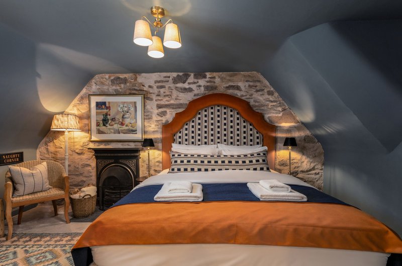 Bedroom with arched headboard, orange throw, fireplace, stone wall and ambient lighting