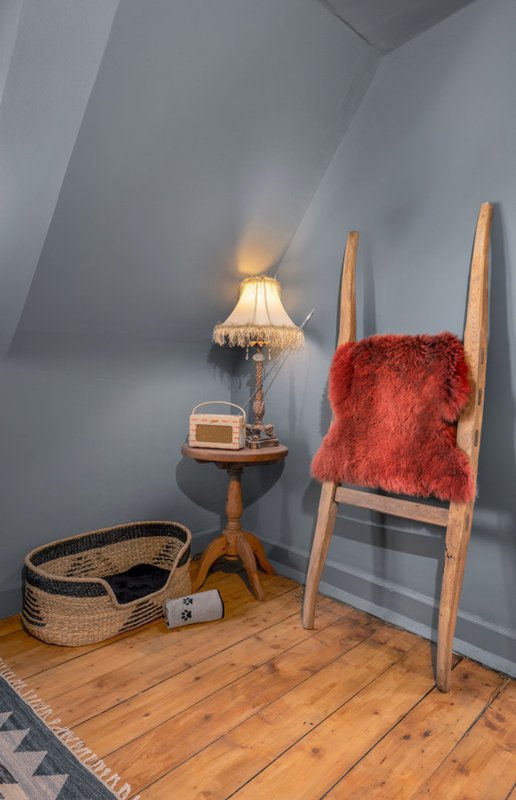 Attic bedroom corner with wooden ladder-back chair, red throw, small side table with lamp, and wicker basket