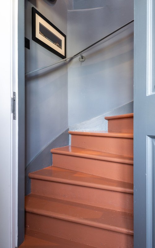 Staircase with orange-red wooden steps, gray walls, handrail, and framed artwork above