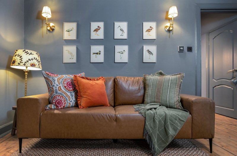 Living room with brown leather sofa, decorative pillows, throw blanket, wall art, and table lamp