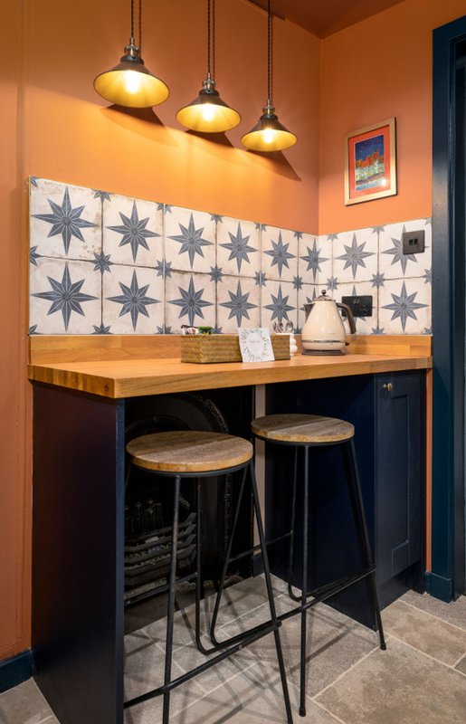 Modern kitchenette with orange walls, pendant lighting, geometric tile backsplash and bar seating