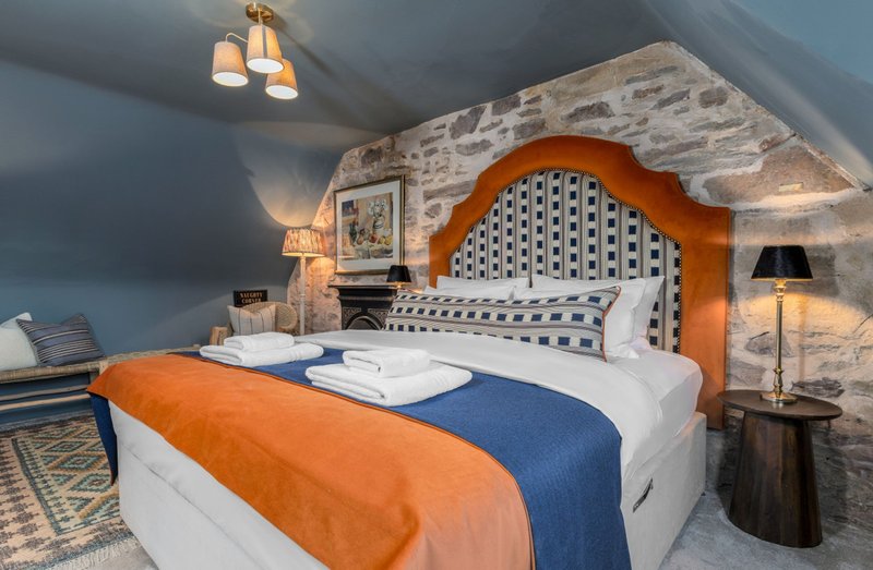 Bedroom with orange wooden headboard, white bedding, blue throw, pendant lighting and stone feature wall