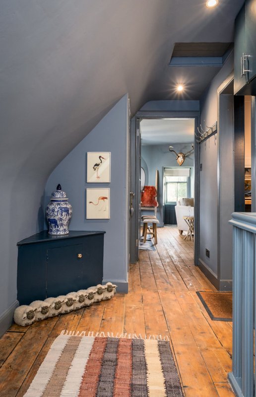 Hallway with wooden floor, framed wall art, dark dresser, and geometric runner rug