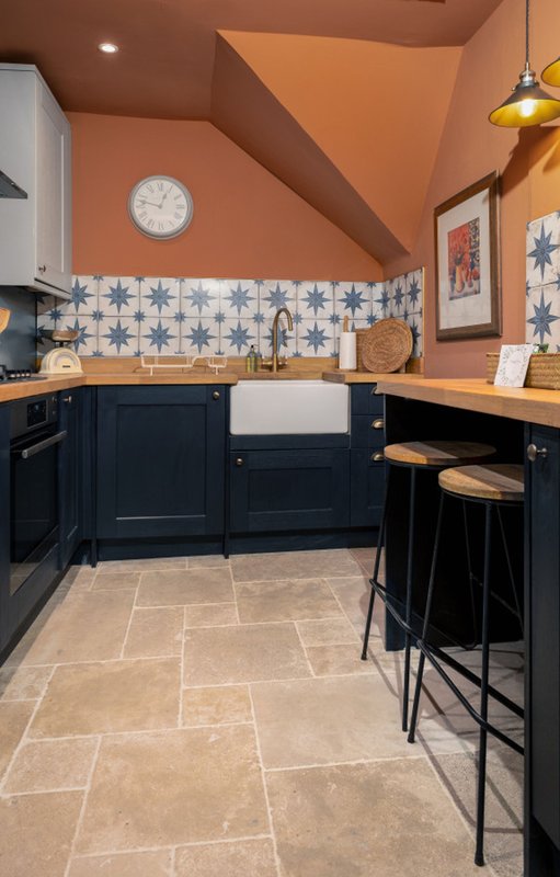 Modern kitchen with navy cabinetry, orange walls, patterned backtile and breakfast bar seating