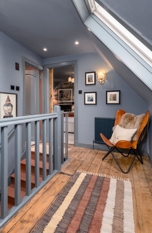 Loft landing with wooden flooring, striped runner rug, orange chair, framed artwork and stair gate