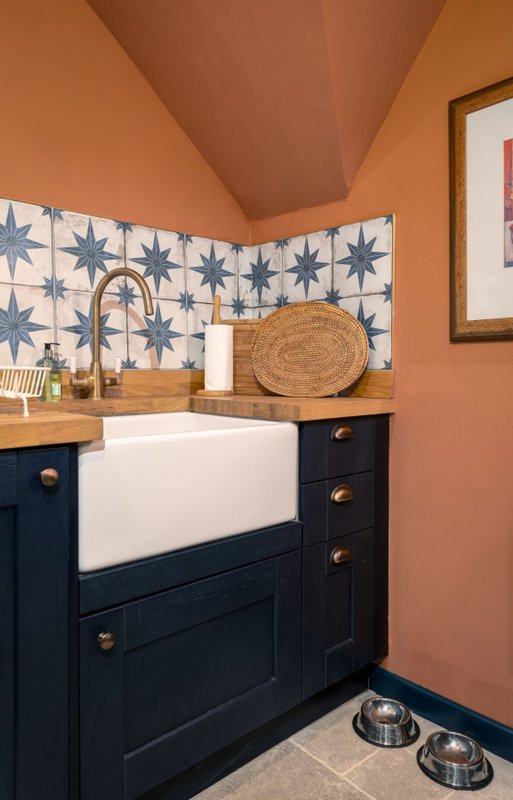 Kitchen corner with navy cabinetry, white farmhouse sink, star-patterned backsplash and terracotta walls