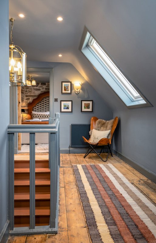 Attic landing with skylight, butterfly chair, framed artwork, and striped runner rug