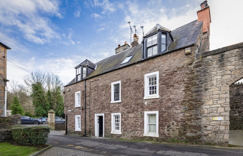 Stone-built residential property with mansard roof, white-framed windows, driveway and front garden