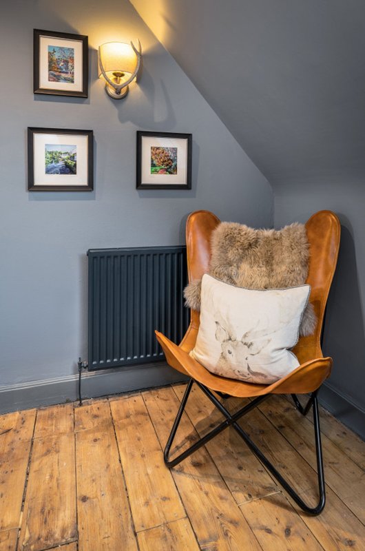 Attic bedroom corner with wooden butterfly chair, cushions, wall sconces and framed artwork