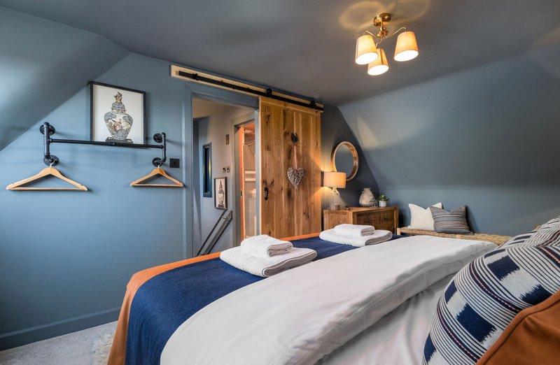 Modern bedroom with blue walls, double bed, wooden wardrobe and ceiling light fixture