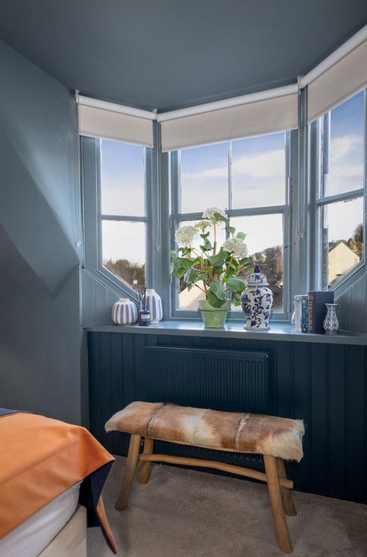 Corner window with potted plant, wooden bench, orange cushion and landscape view