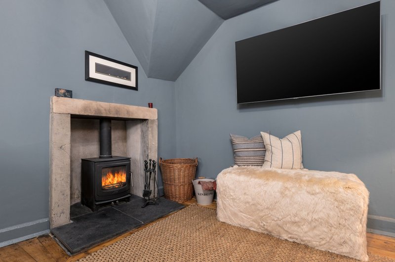 Modern bedroom with wood-burning stove, cream upholstered bed, wall-mounted TV and framed artwork