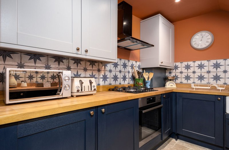 Modern kitchen with blue cabinetry, wooden countertop, patterned tile backsplash and white appliances