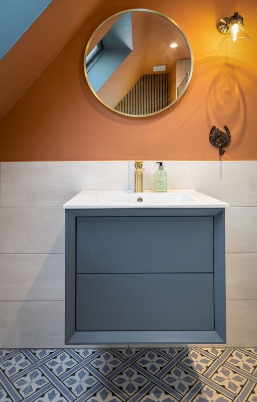 Modern bathroom with circular mirror, blue vanity unit, and patterned floor tiles