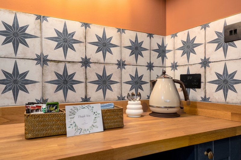 Kitchen counter with wooden surface, star-patterned tile backsplash, kettle and decorative items