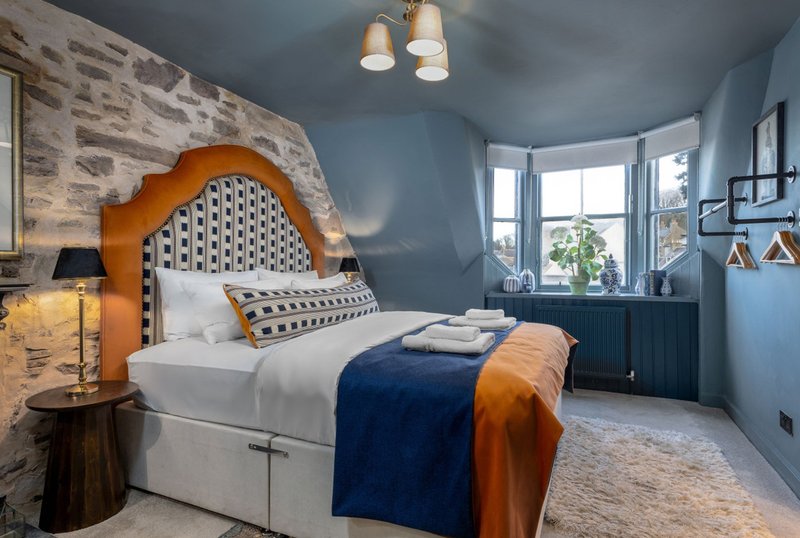 Modern bedroom with orange and blue headboard, white bedding, pendant lights and brick accent wall