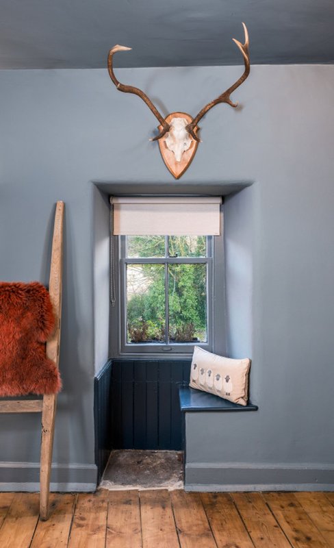 Modern hallway with mounted deer antlers, window seat, wooden floor and fur throw
