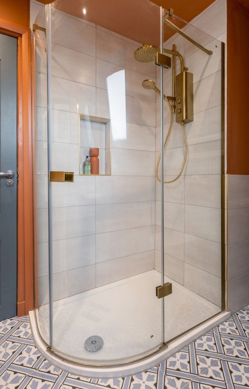 Modern bathroom with walk-in shower, glass enclosure, brass fixtures and patterned floor tiles
