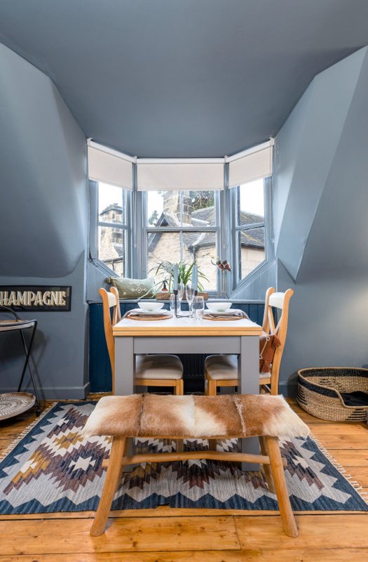Bright attic bedroom with sloped ceiling, bay window, wooden table and chairs, geometric rug