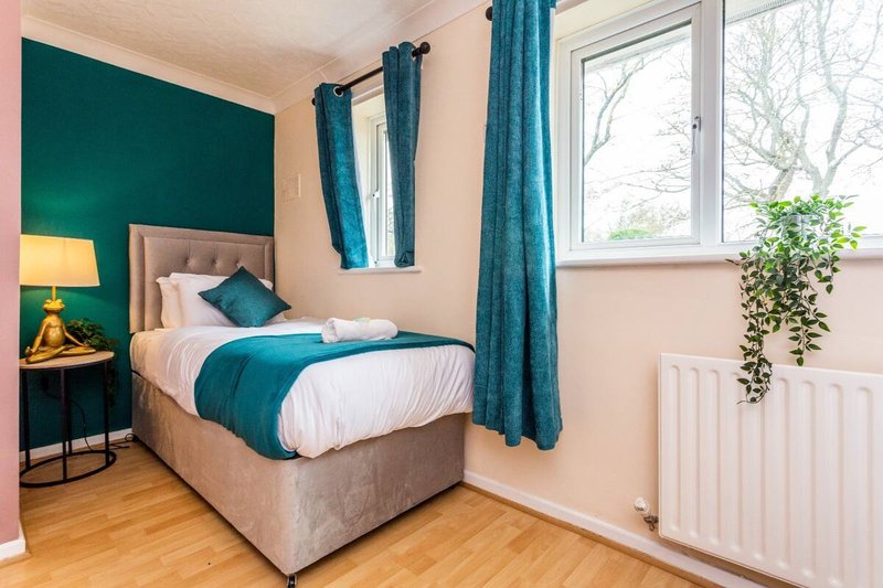 Bedroom with single bed, teal headboard, matching curtains, wooden floor and bedside lamp