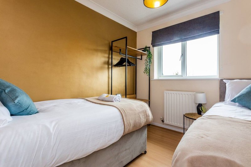 Twin bedroom with mustard-yellow accent wall, two beds with white linens, and window with blinds
