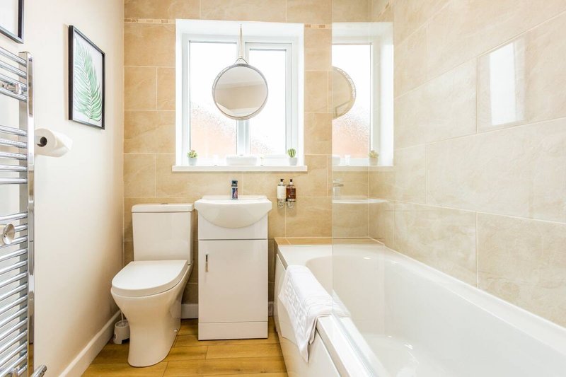 Modern bathroom with toilet, vanity sink, bathtub, and window with circular mirrors