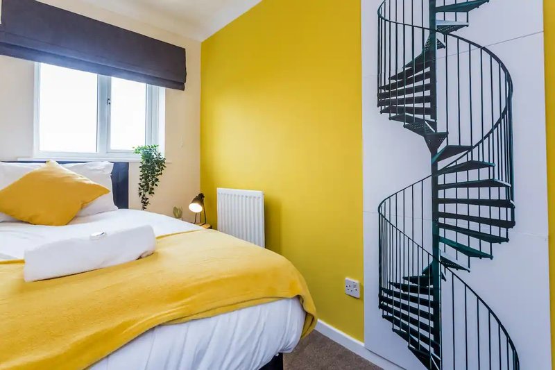 Bright bedroom with yellow accent wall, double bed with yellow bedding, window, and spiral staircase