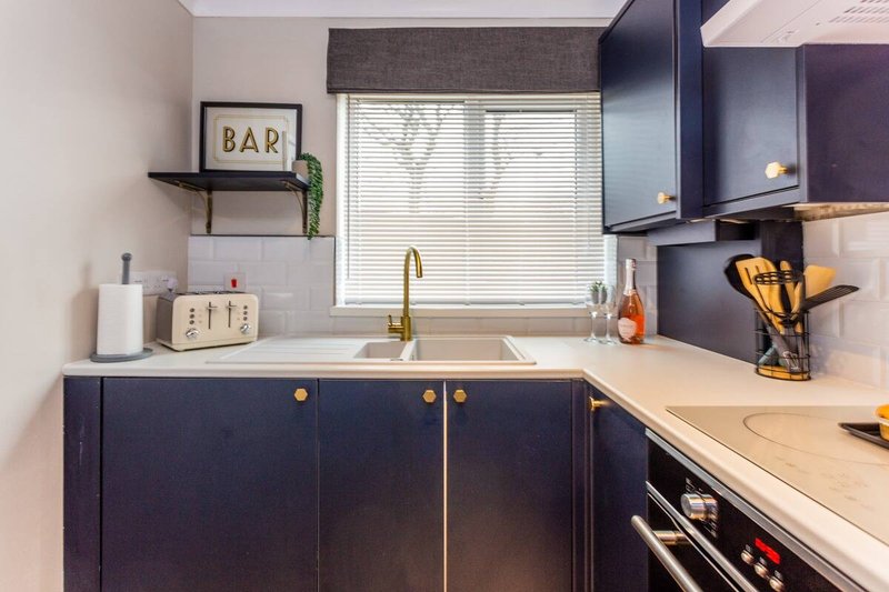 Modern kitchen with dark cabinetry, white countertop, sink, and decorative bar sign