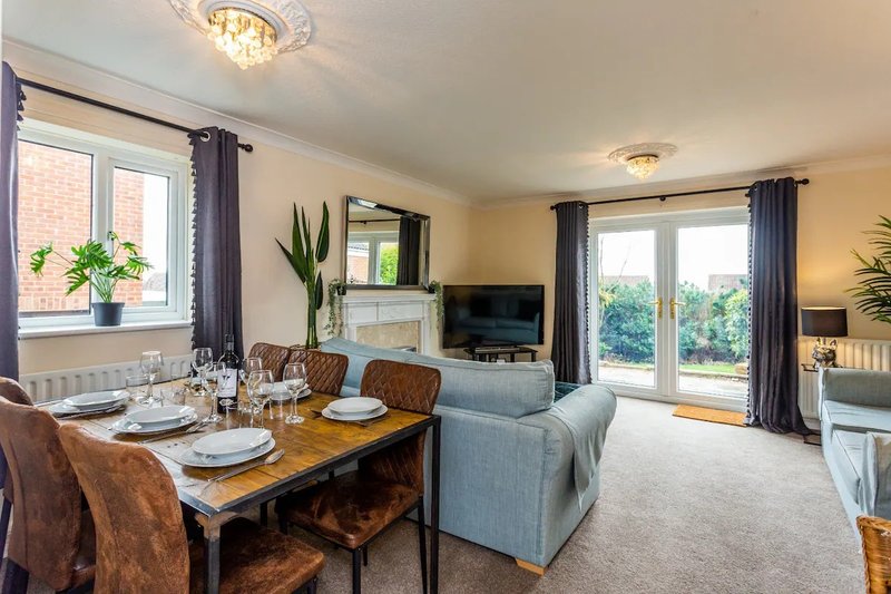 Open-plan living and dining area with wooden table, upholstered sofa, TV, and garden views
