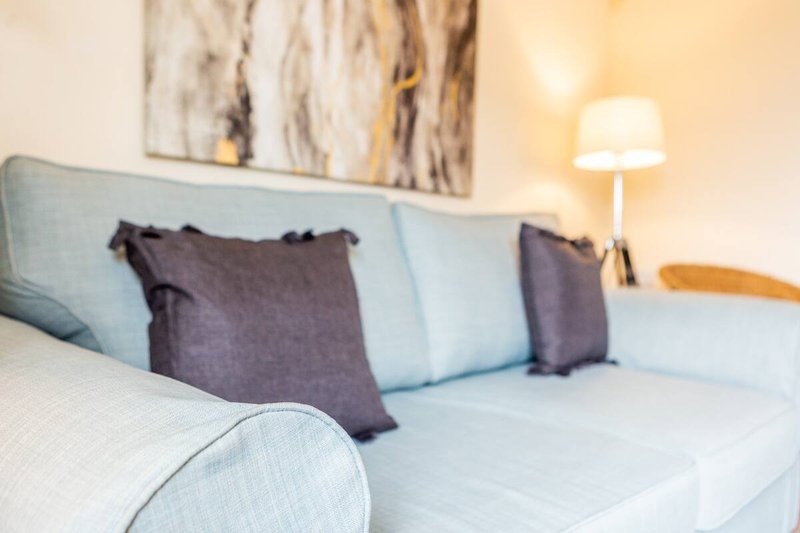 Light blue upholstered sofa with dark cushions, abstract wall art, and table lamp
