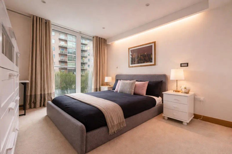 Modern bedroom with gray upholstered bed, black bedding, white nightstands and floor-to-ceiling windows