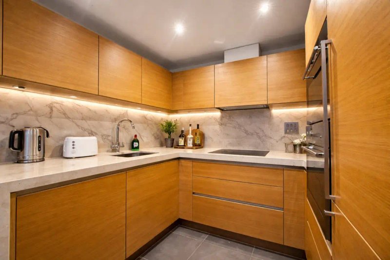 Modern kitchen with wooden cabinets, marble backsplash, stainless steel appliances and countertop items