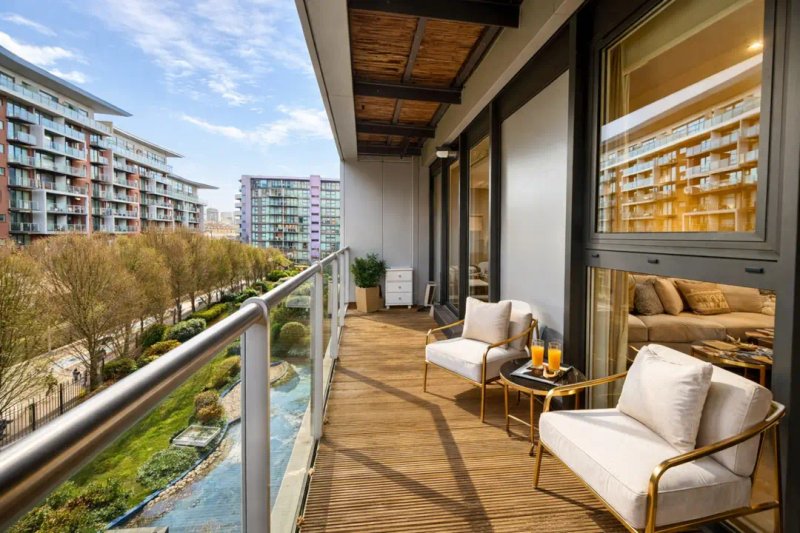 Modern balcony with two cream armchairs, wooden decking, and city views