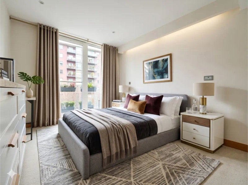 Modern bedroom with double bed, decorative pillows, wooden nightstands and large windows overlooking city