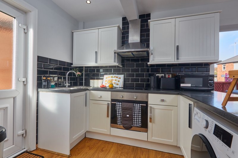 Modern kitchen with white cabinetry, black tile backsplash, stainless steel appliances and wooden floor