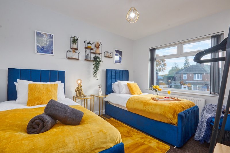 Bright twin bedroom with blue upholstered beds, yellow bedding, and large window with street view