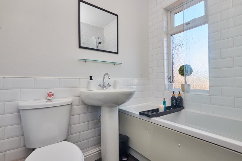 Modern bathroom with white subway tiles, pedestal sink, toilet, bathtub and mirror