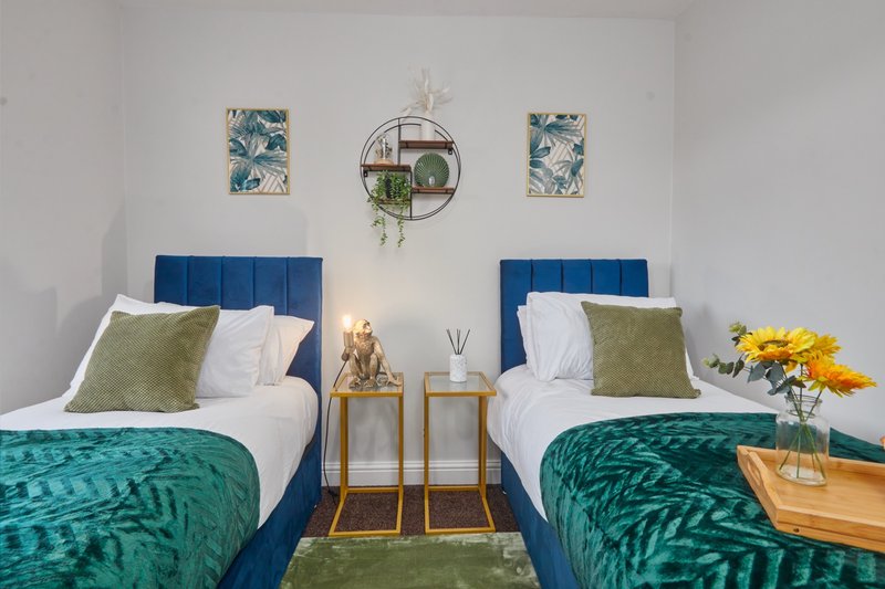 Twin bedroom with blue headboards, green bedding, wooden side tables and wall art