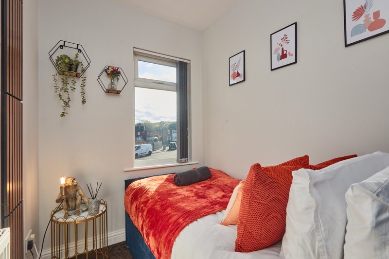 Modern bedroom with double bed, red bedding, wall art, hanging plants and window view